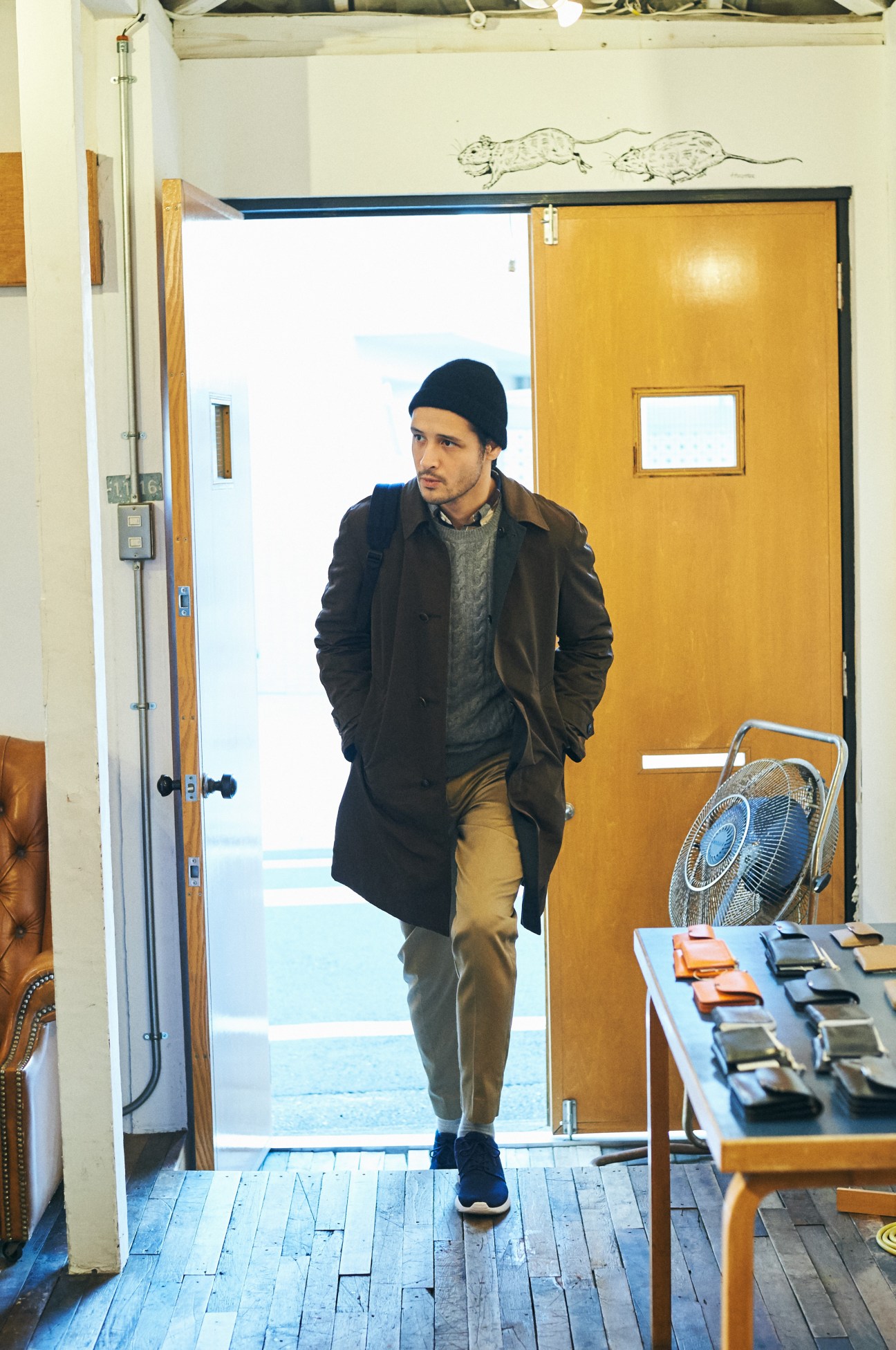 Man wearing Boglioli coat and Kaptain Sunshine knit hat standing in doorway with yellow door.