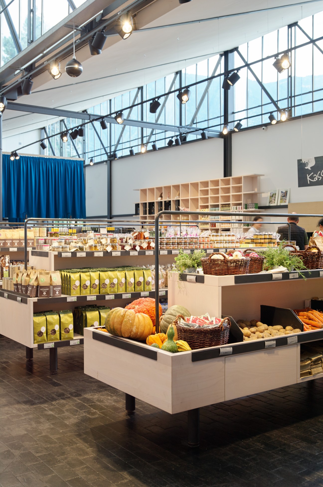 Modern grocery store interior with industrial ceiling, produce displays, and wicker baskets in Lana