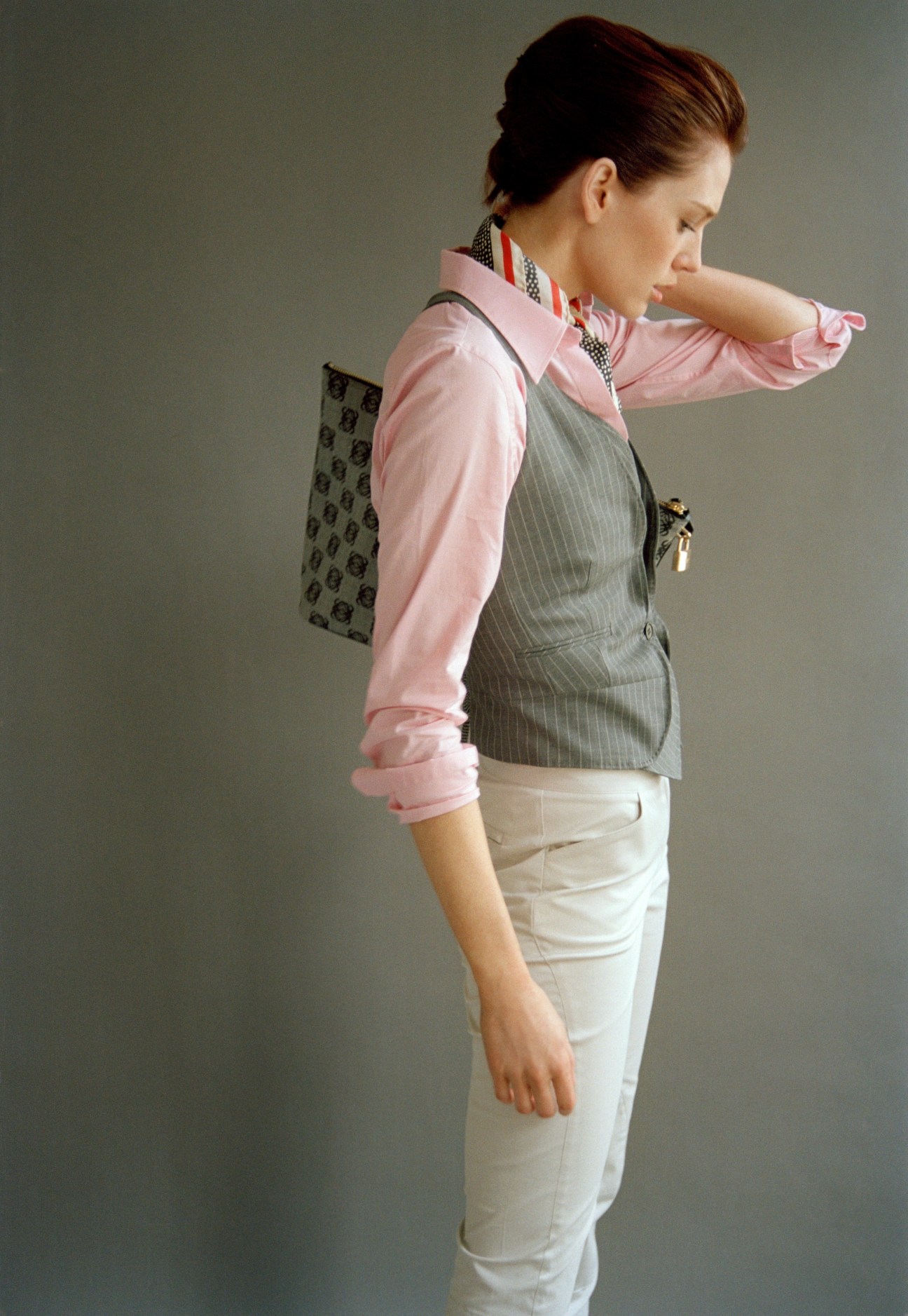 Model wearing pink shirt, gray pinstriped waistcoat, white trousers, patterned scarf, and holding a Loewe bag.