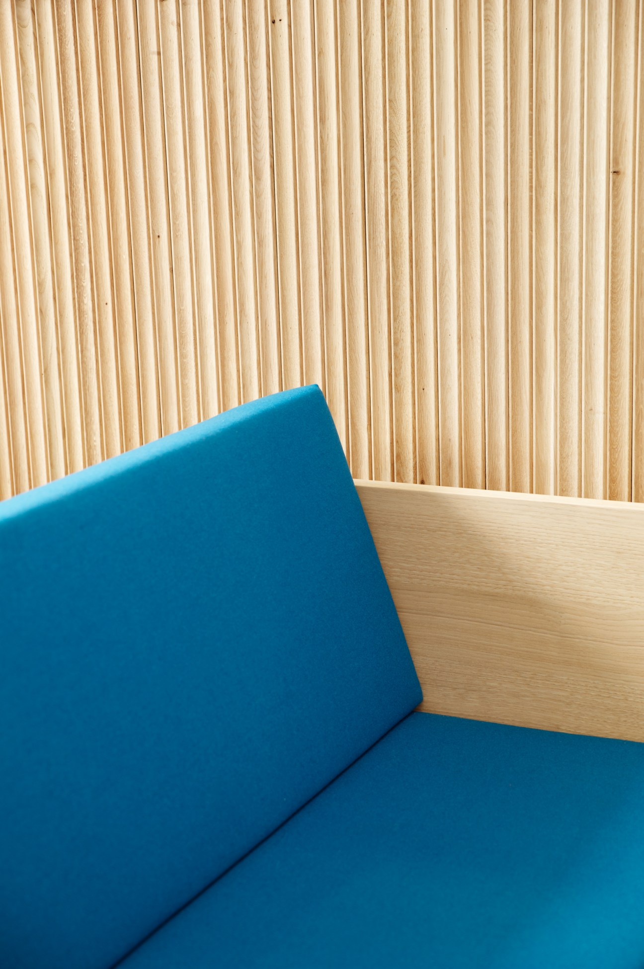 Blue upholstered chair with wooden backrest against natural wood slat wall