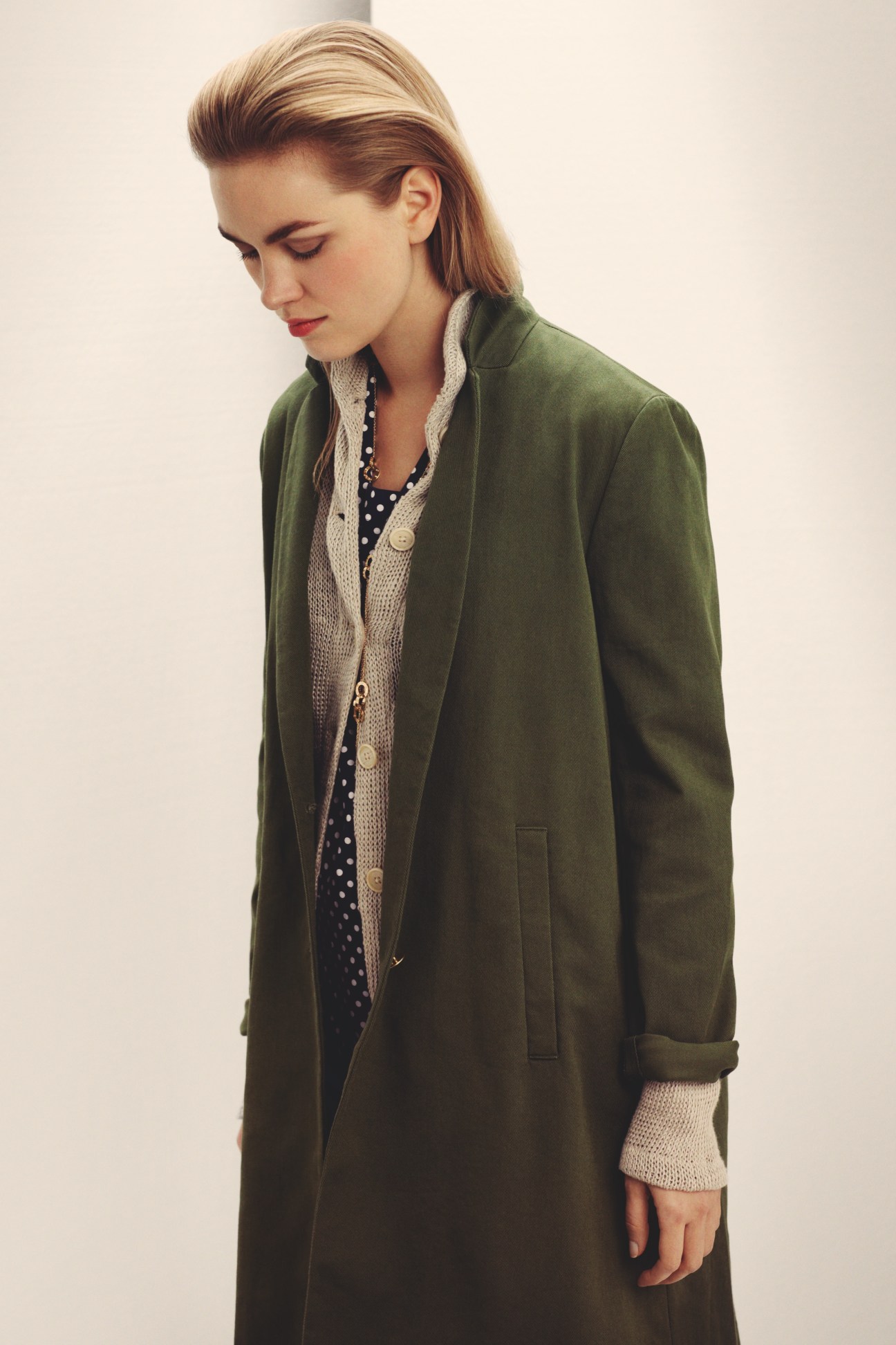 Woman wearing a green Barena coat layered over a cardigan and patterned shirt, accessorized with a Cartier necklace.