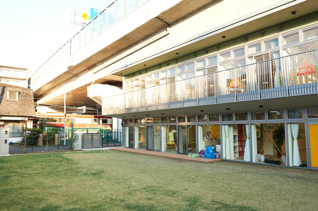 Byobugaura Harukaze Nursery exterior with grassy play area beneath an elevated highway overpass.