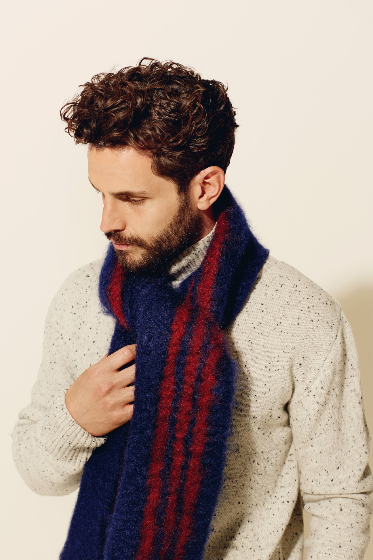 Man wearing cream knit sweater with navy and red striped mohair scarf.