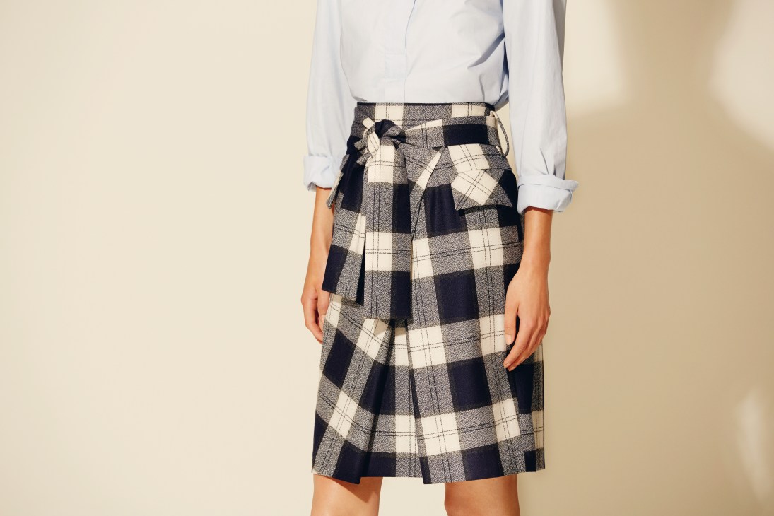 Woman wearing a white collared shirt tucked into a black and cream tartan wool skirt with a belt.