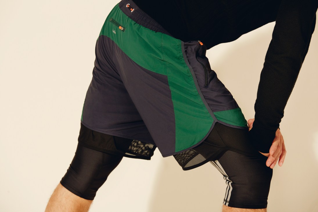 Person wearing Adidas Coolmax top and black shorts with mesh paneling against cream background.