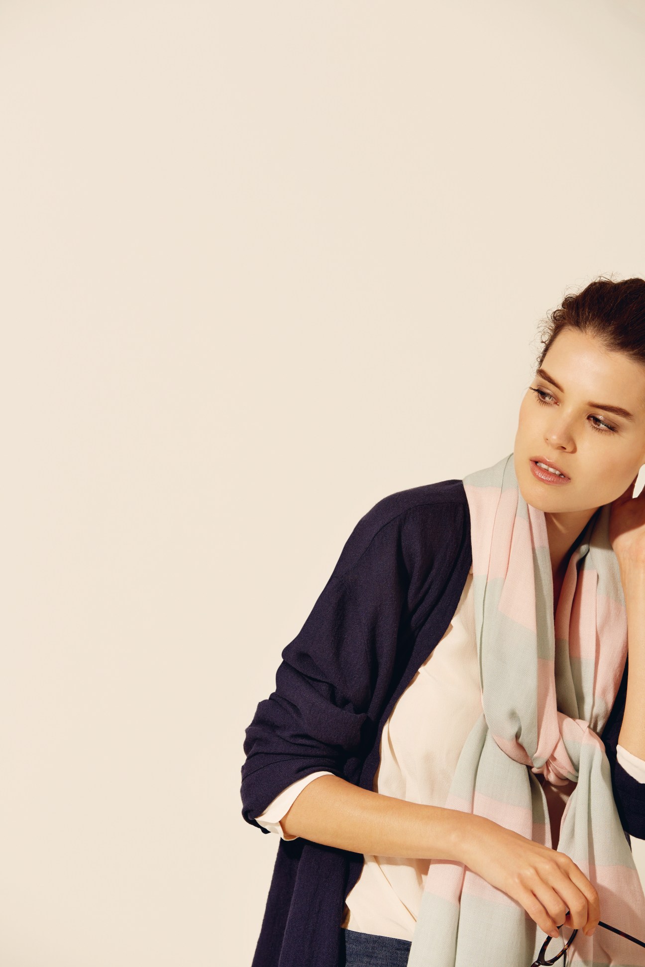 Woman wearing a navy cardigan layered over a cream top with a pink and grey striped scarf.