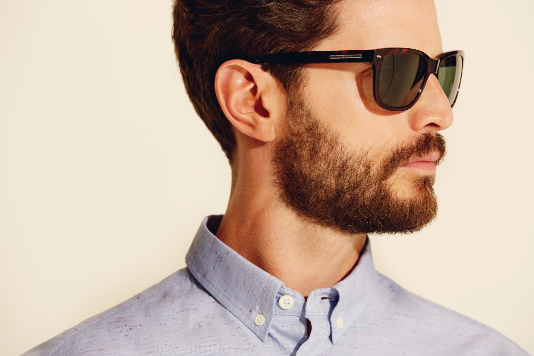 Man wearing tortoiseshell sunglasses with Zeiss lenses and a light blue button-up shirt.