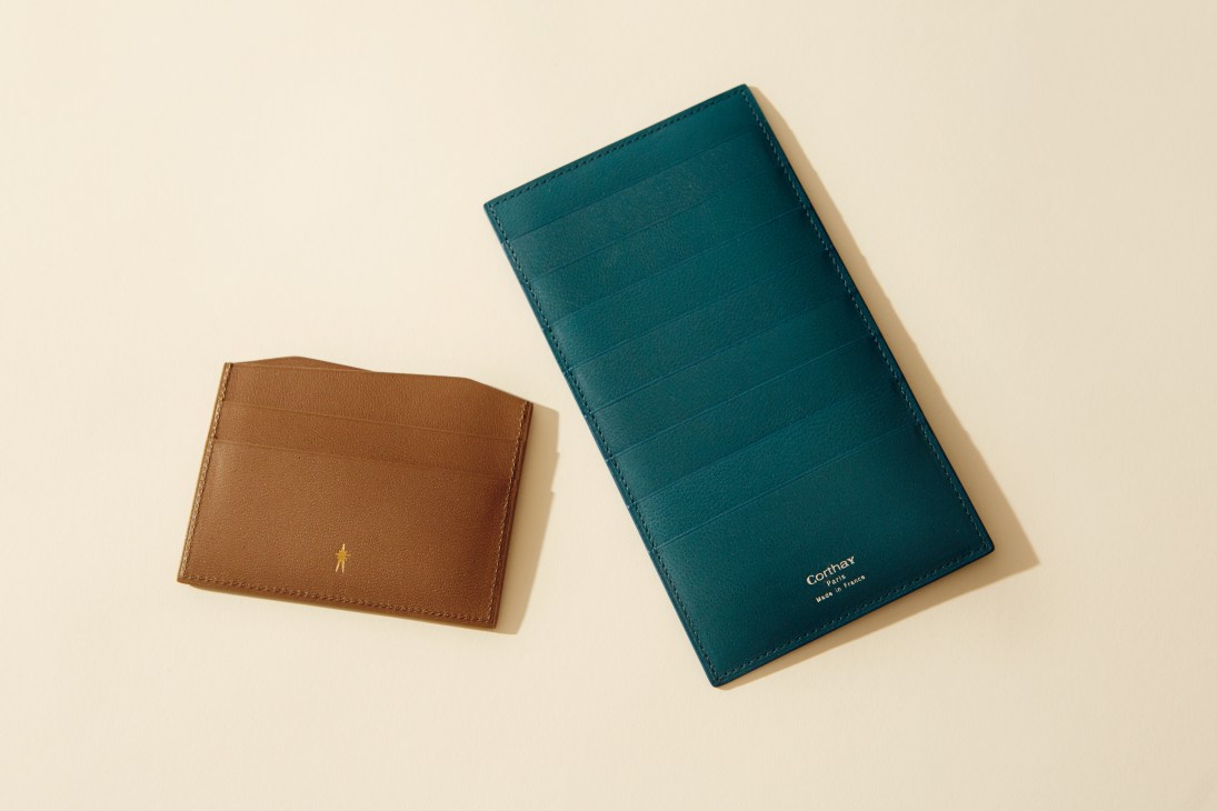 Corthay brown leather card holder and teal crocodile skin wallet on cream background.