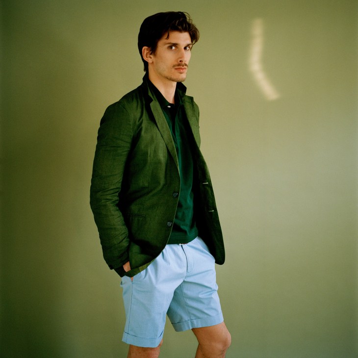 Man wearing a green Burberry Prorsum jacket, Brooks Brothers polo shirt, Incotex shorts, and Paul Smith belt against a green background.