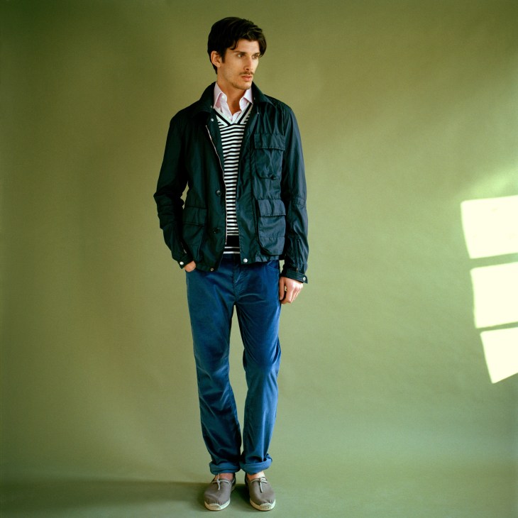 Male model wearing CP Company jacket, Bamford & Sons jumper, Loewe shirt, Trussardi 1911 trousers, and Hermès shoes against yellow-green background.