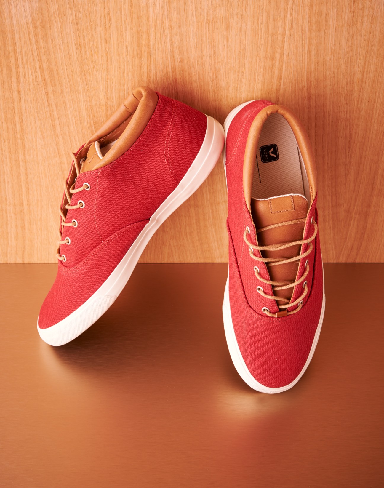 Pair of red canvas sneakers with white sole and tan leather accents on wooden background.