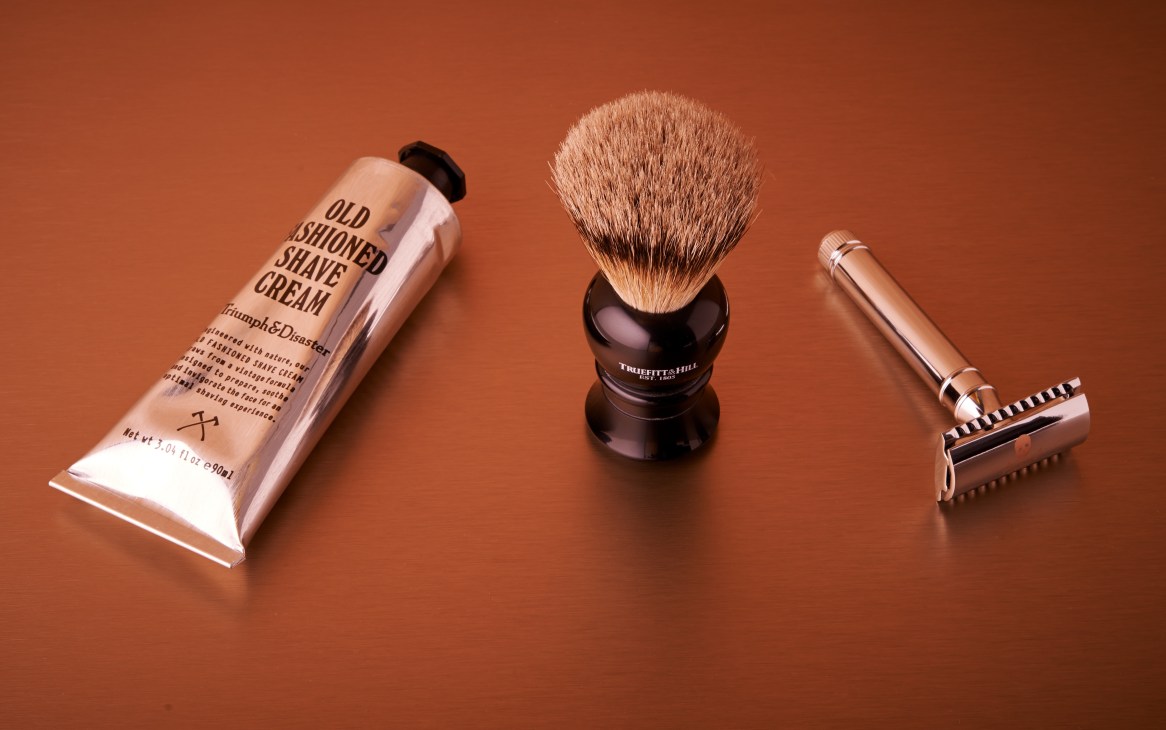 Triumph & Disaster shaving cream, Truefitt and Hill badger-hair brush, and Bluebeard's Revenge razor on terracotta background.