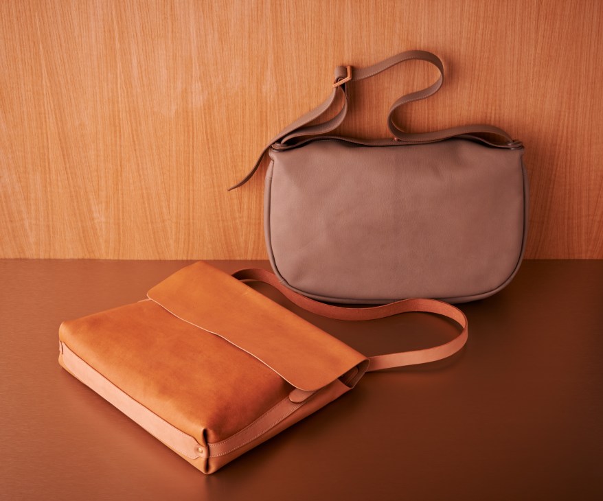 Two leather shoulder bags in tan and grey displayed on an orange wooden surface.