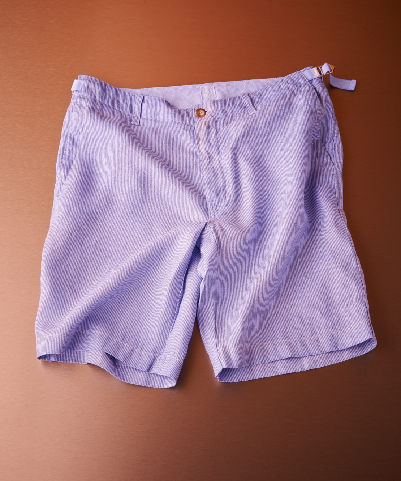 120% Lino lightweight striped shorts in lavender linen against a rust-colored background.