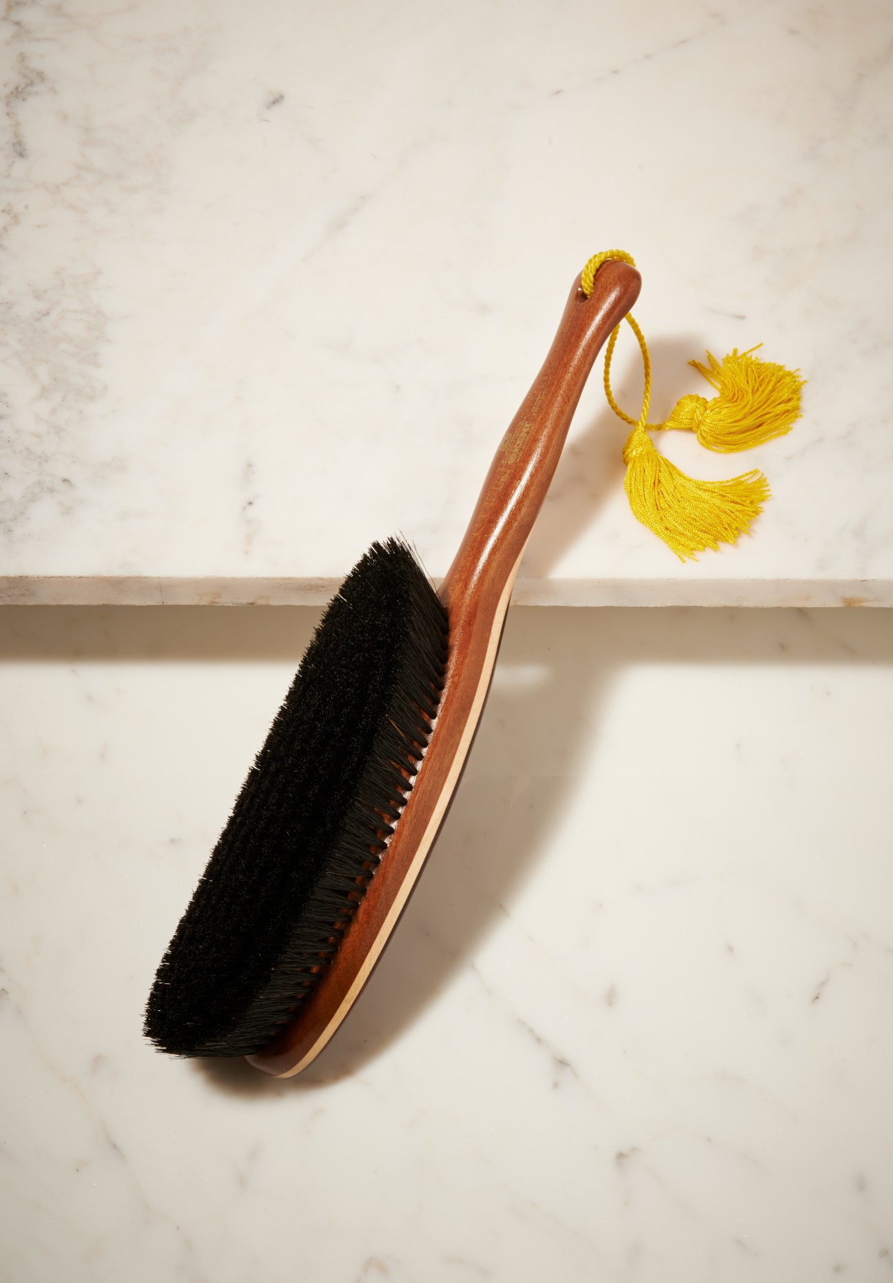 Kent wooden clothes brush with black bristles and yellow tassel detail on marble surface.