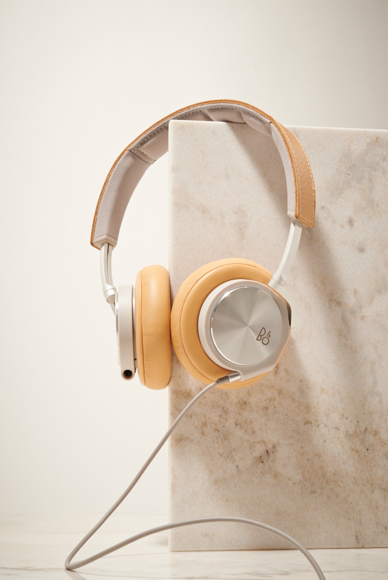 B&O PLAY H6 headphones in tan and white with leather headband on marble block.