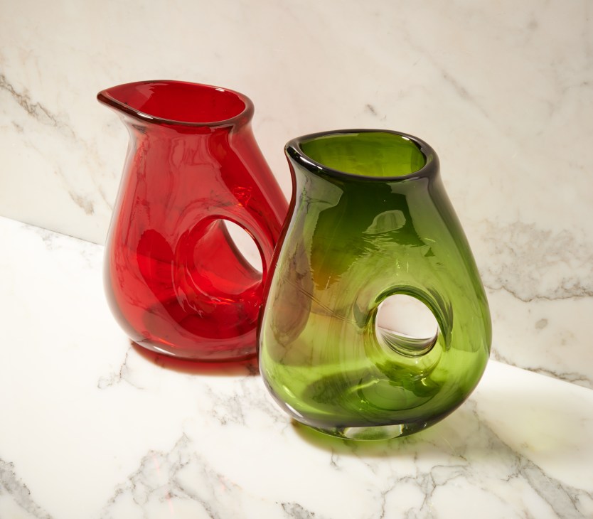 Two mouth-blown glass jugs by Pols Potten in red and green on a marble surface.