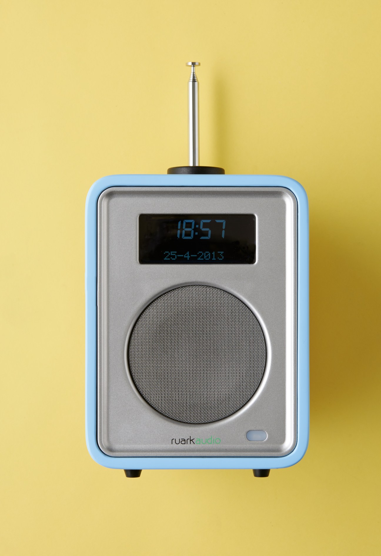 Ruark R1 portable radio with blue casing, silver face, and digital display on yellow background.