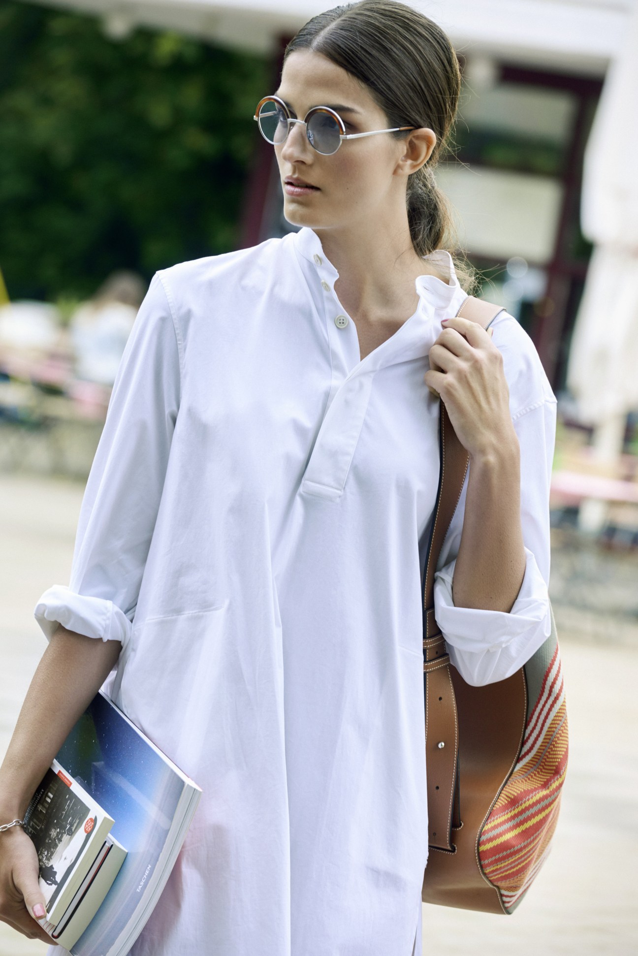 Woman in white shirt dress and round sunglasses holding magazines outdoors.