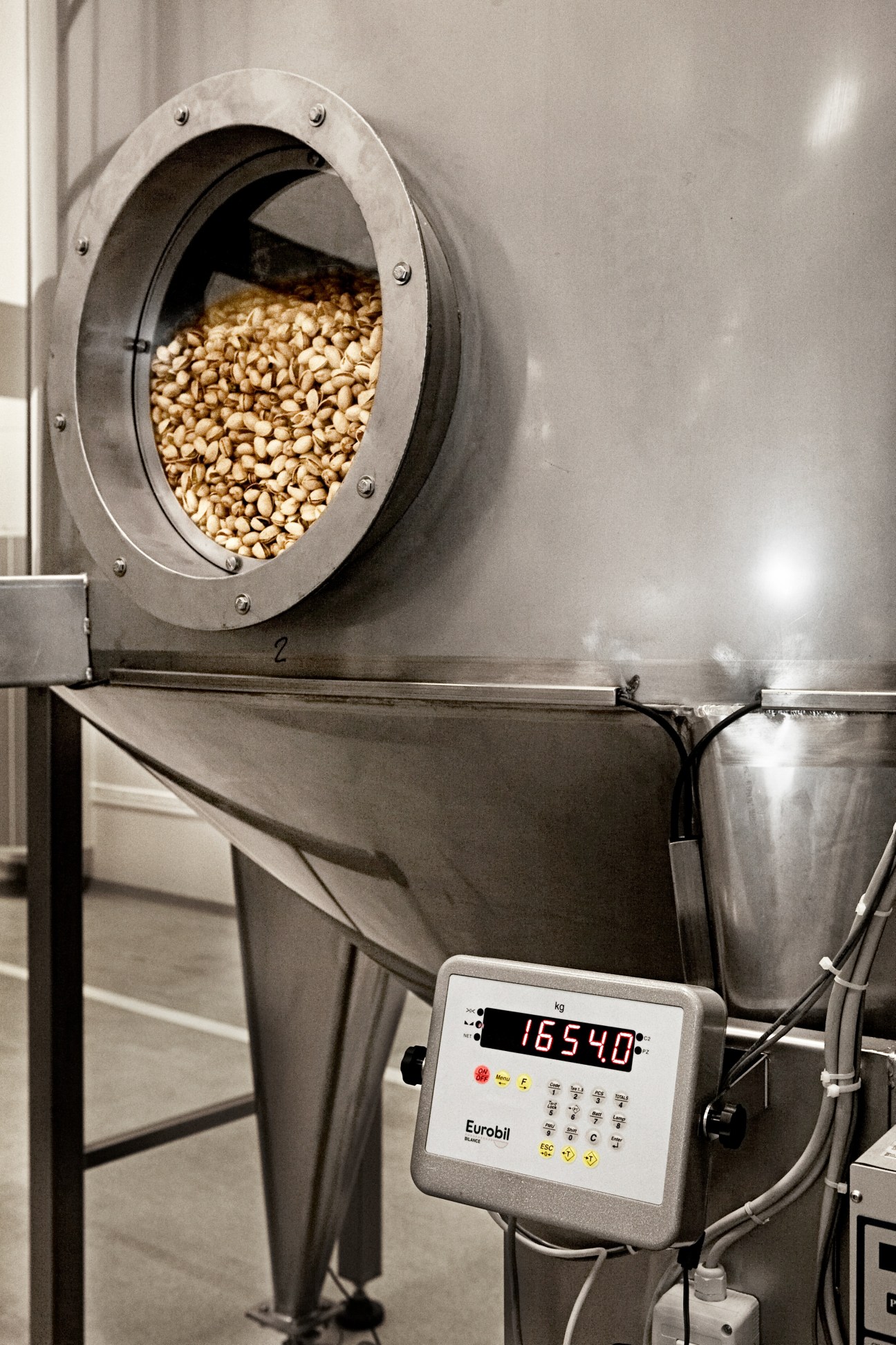 Industrial buffer silo filled with nuts, with a Eurobil digital scale display showing weight.