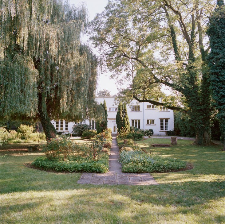 Villa St Martin's white Bauhaus-style rear façade viewed through a tree-lined garden path.