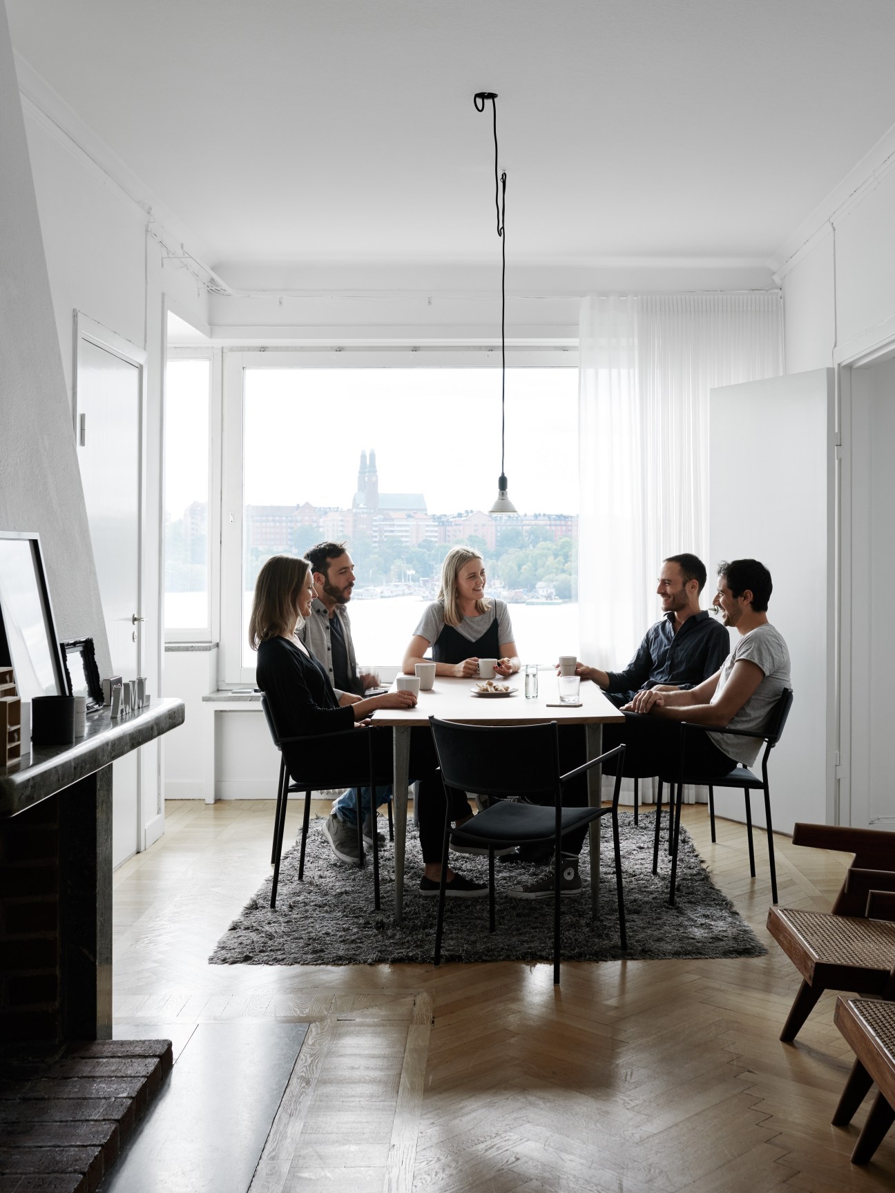 Five people sitting around white table in bright office space with large windows overlooking Stockholm cityscape