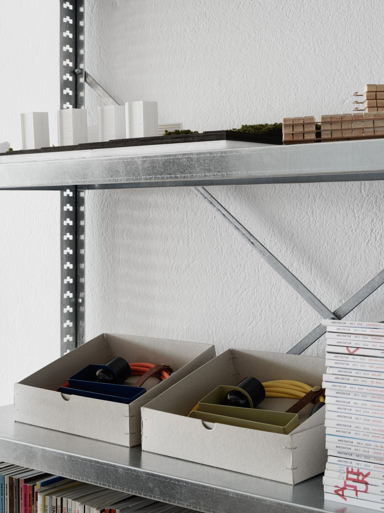 White storage boxes containing AML Clamp Lamps on metal shelving with architecture magazines stacked nearby