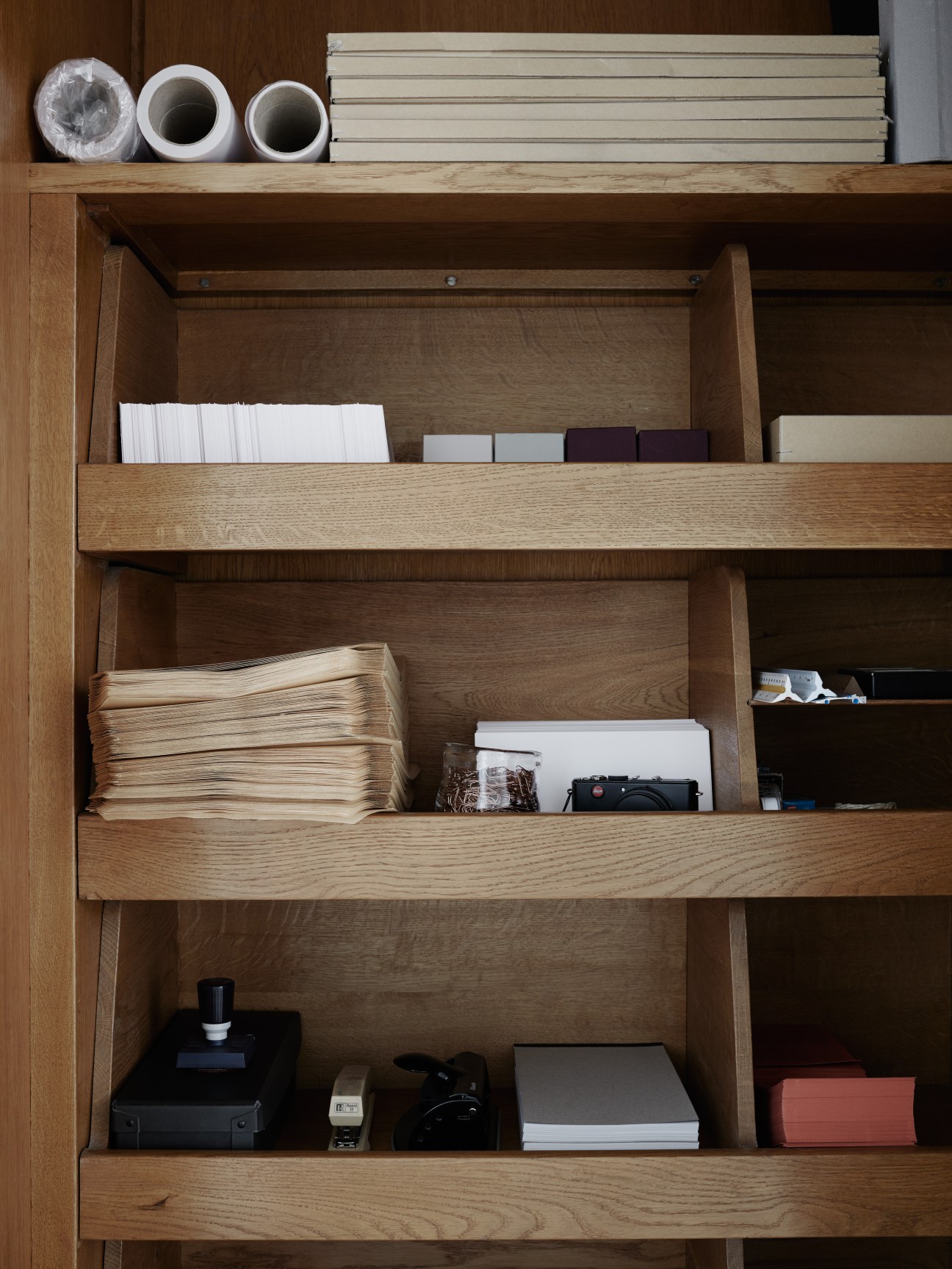 Wooden shelving unit with stacked papers, books, and office supplies arranged on multiple levels