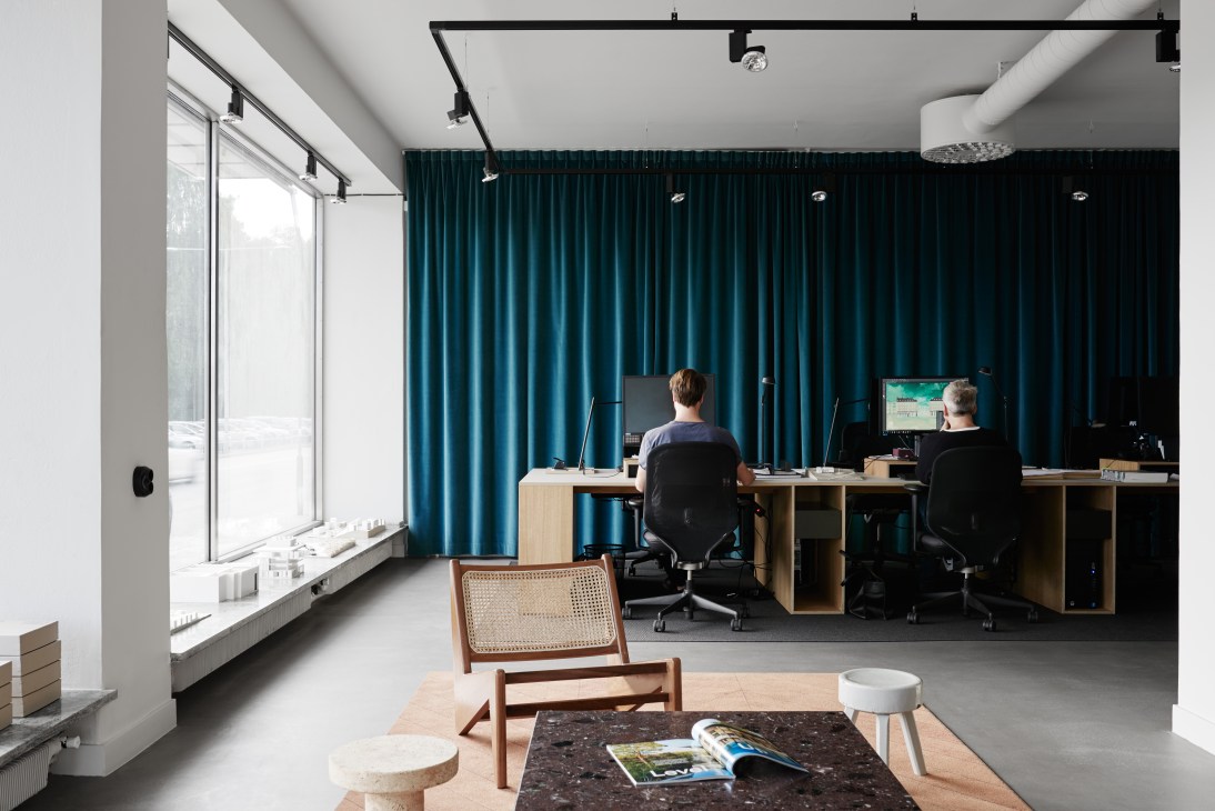 Modern office interior with floor-to-ceiling windows, teal curtains, and two people working at wooden desks