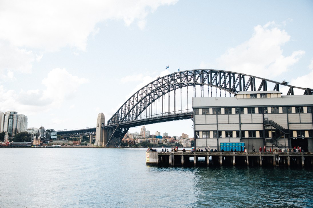 Sydney Harbour Bridge arching over water with The Wharf building in the foreground.