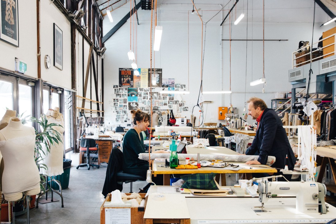 Two people examining fabric swatches at a workbench in a bright theatre costume workshop.