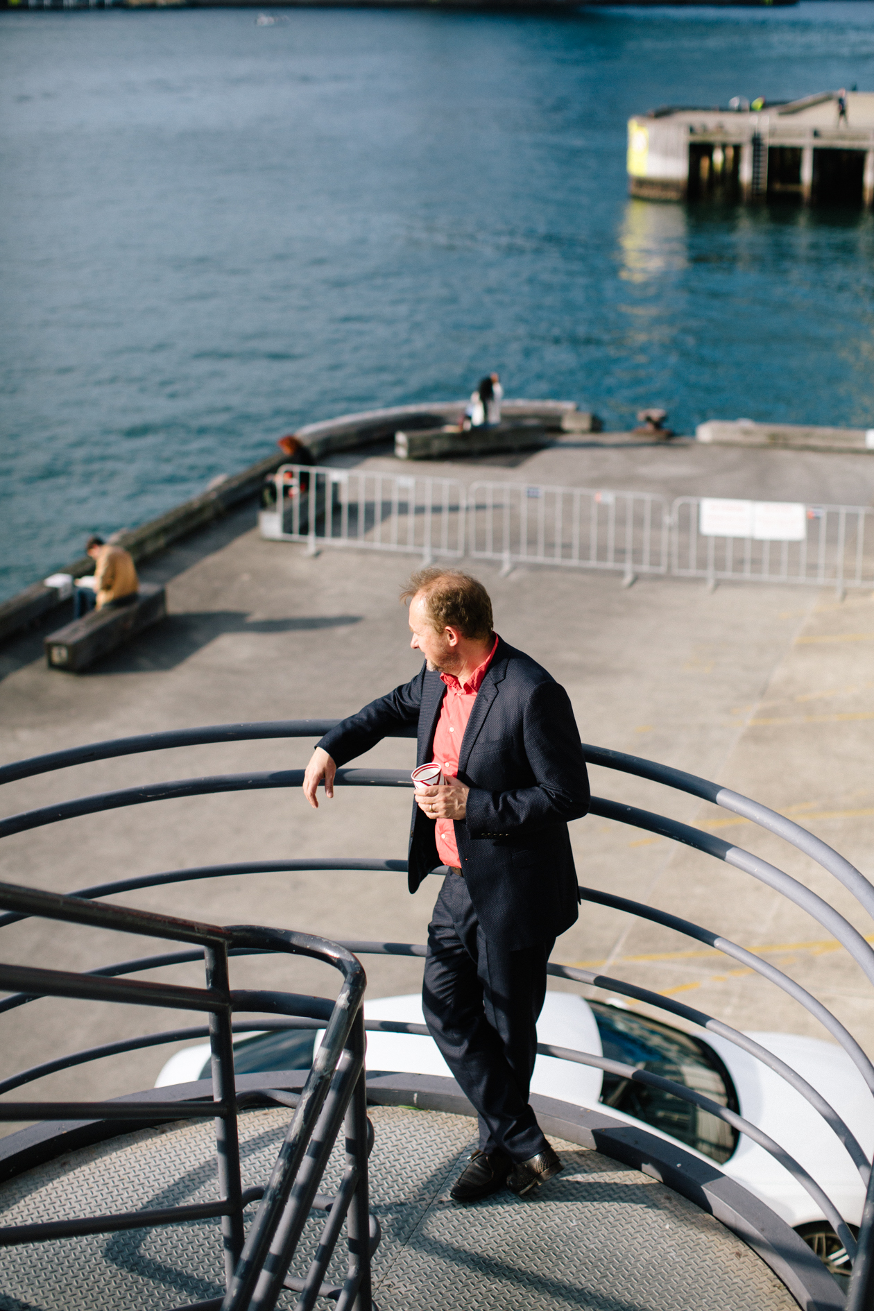 Andrew Upton standing on The Wharf overlooking Sydney Harbour with boats and water visible behind him.