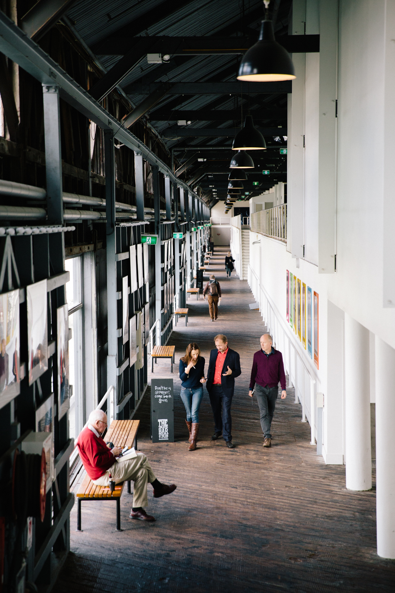 People walking through a modern corridor at Sydney Theatre Company's The Wharf building with black and white walls and pendant lighting.