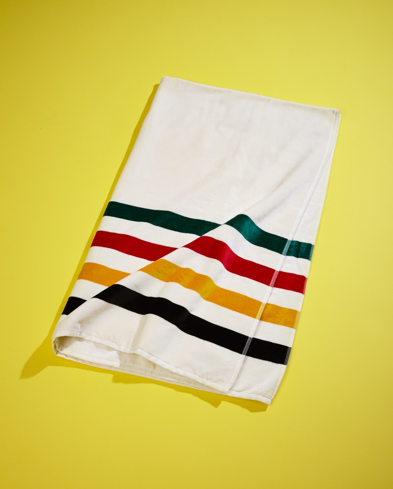 Pendleton striped beach towel with cream, black, gold, red and teal stripes on yellow background.