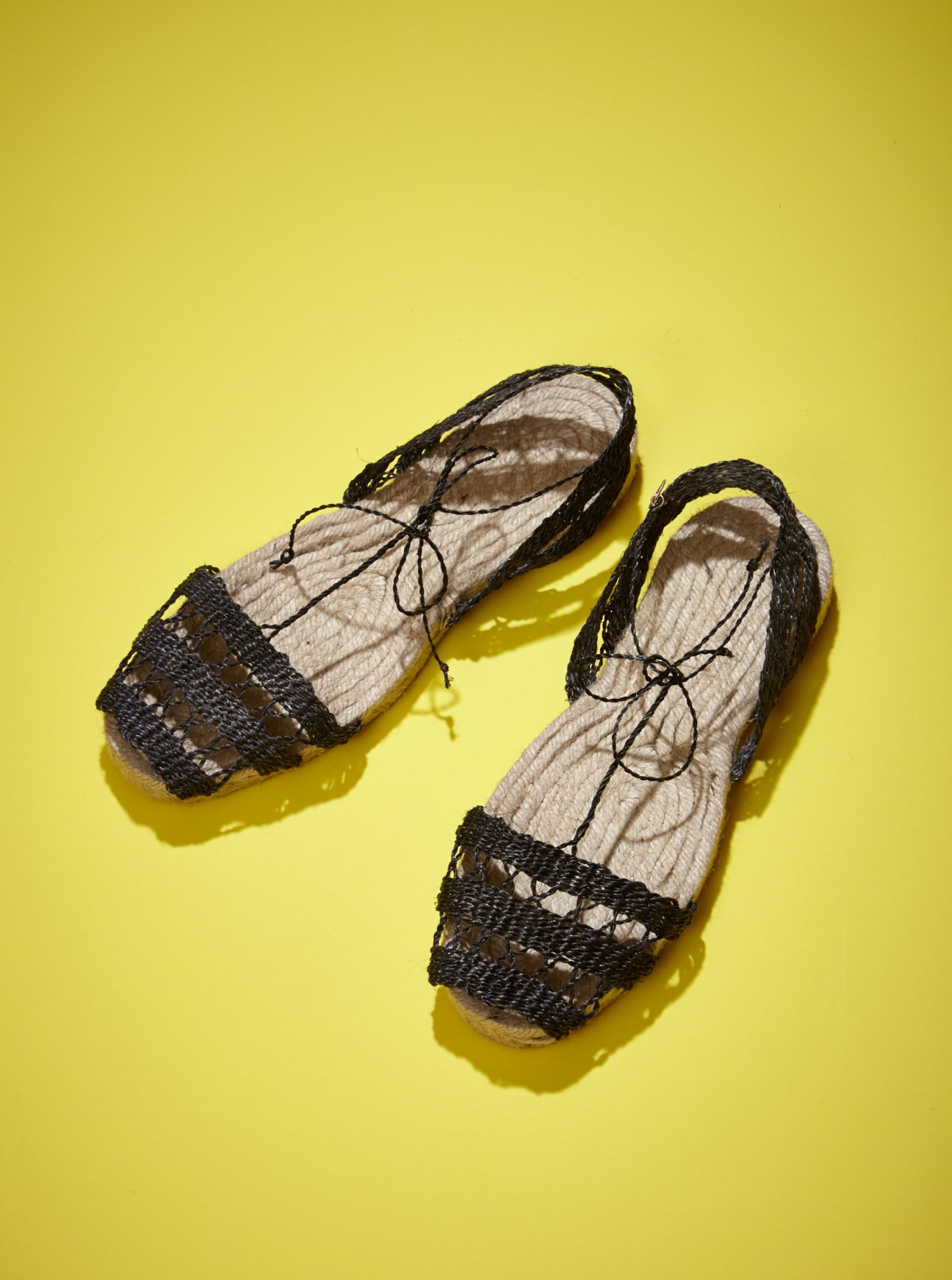 Pair of open-toed black and cream espadrille sandals with drawstring closures on a yellow background.