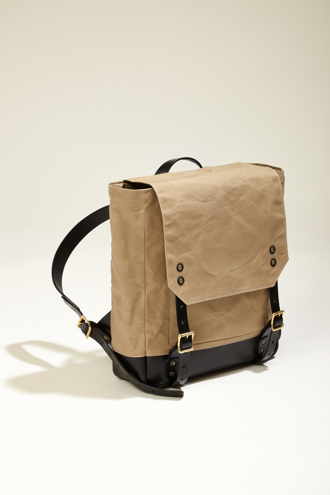 A beige and black canvas rucksack with black leather straps and brass buckles.