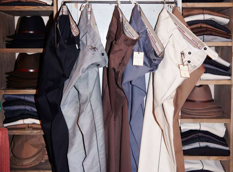 Horsemen's trousers hanging on a rail in Le Gardian's shop, with shelves of folded garments behind.