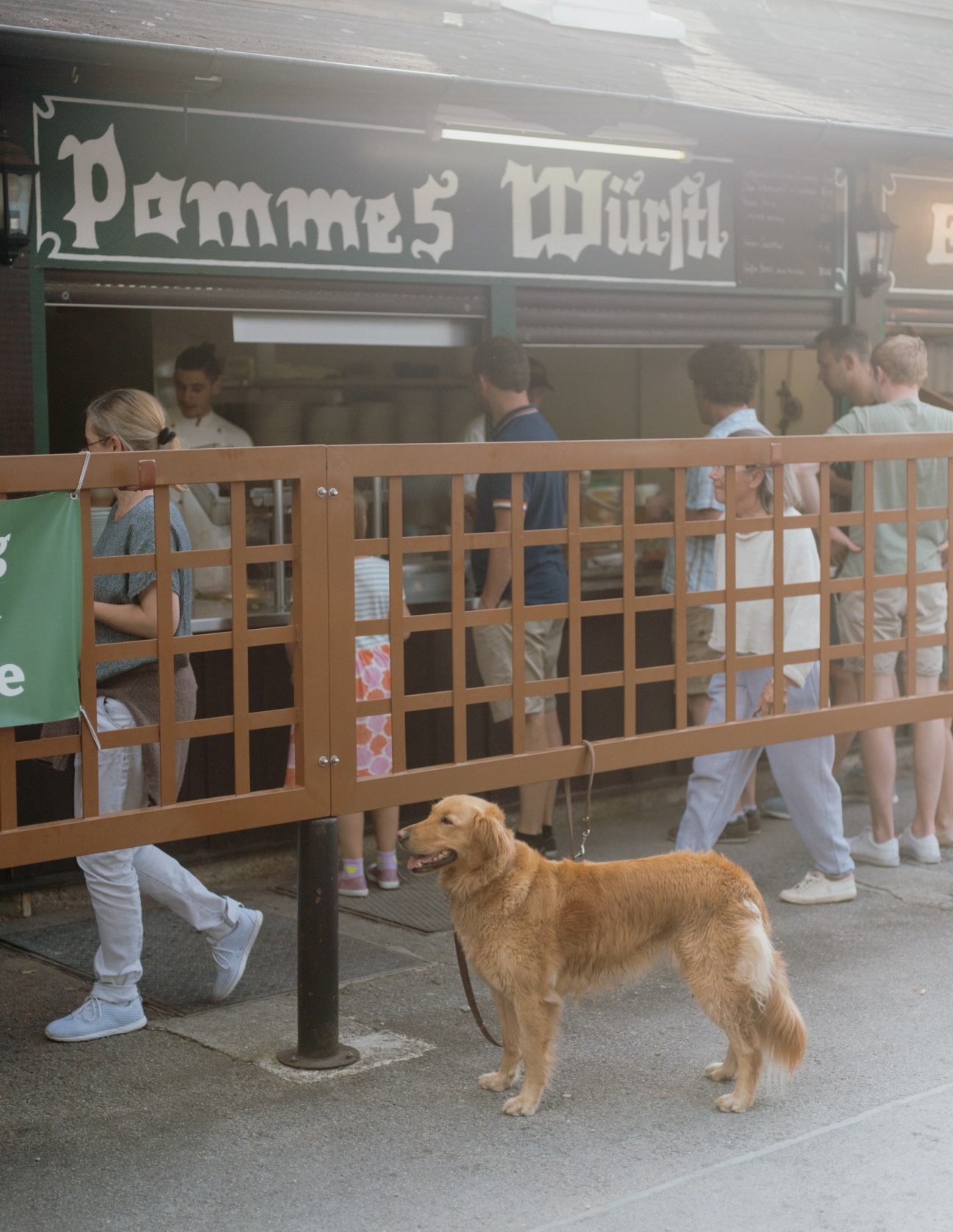 A golden retriever stands on a pavement outside a Munich beer garden service counter.