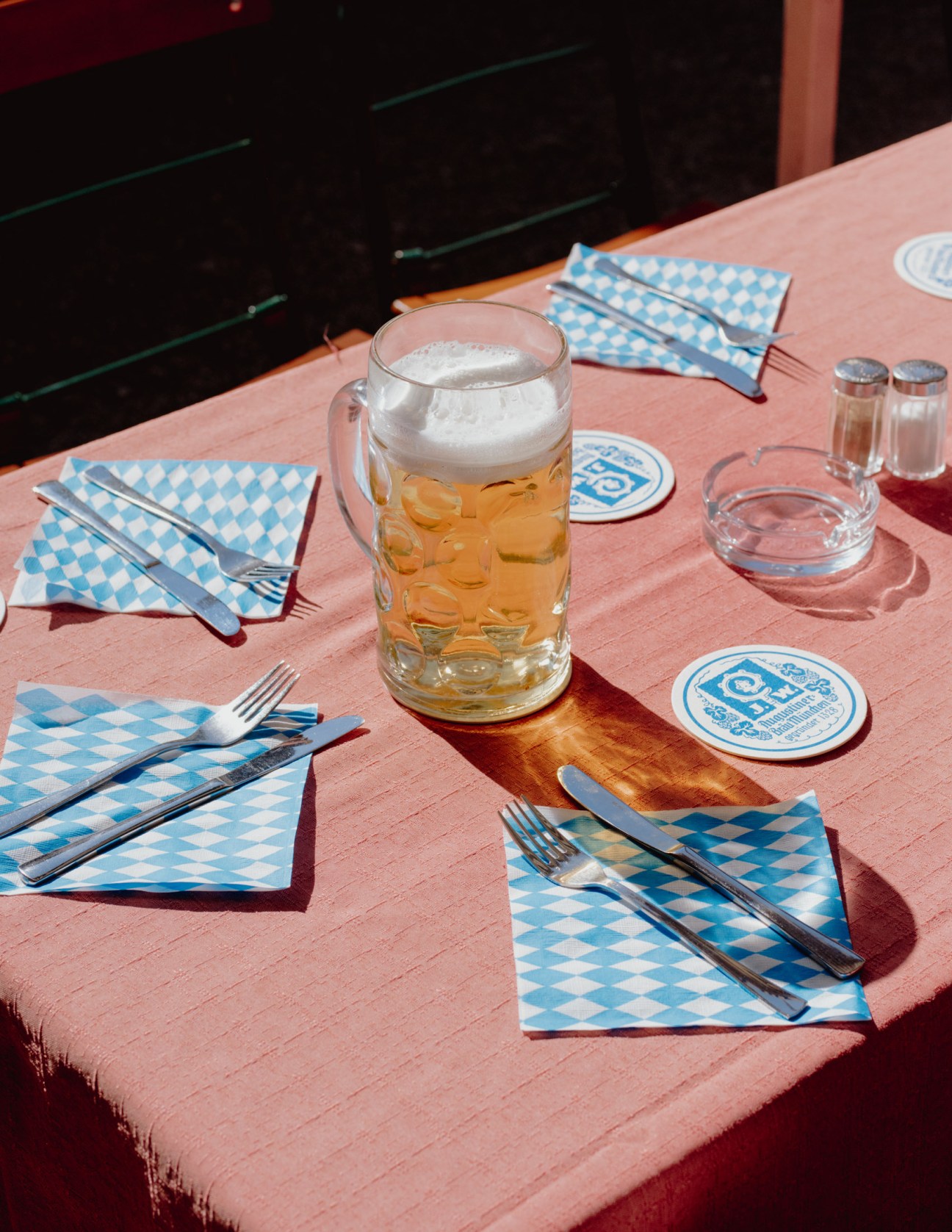 A one-litre beer mug with foam head sits on a pink table with blue checkered napkins and place settings at a Bavarian beer garden.