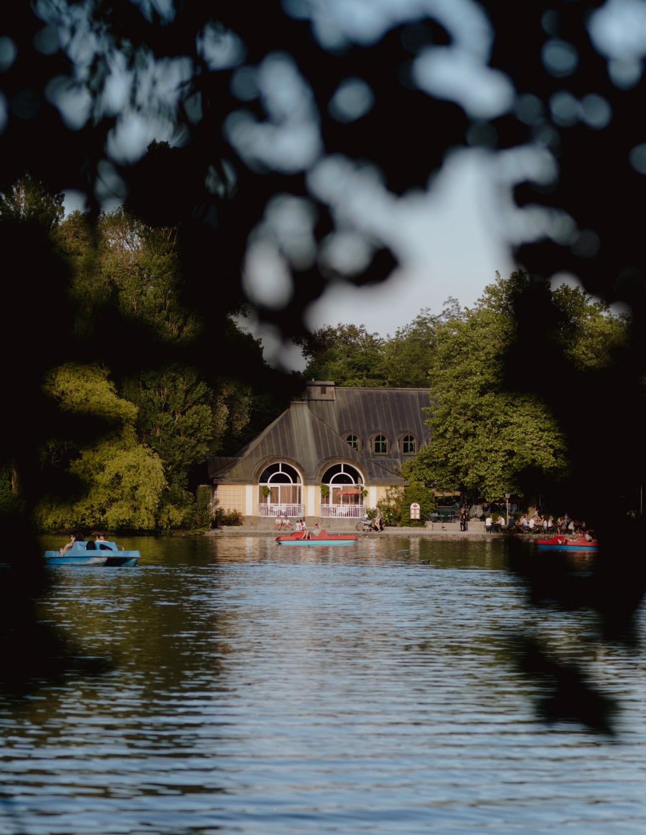 Seehaus beer garden viewed from the lake with boats and dappled tree shadows overhead