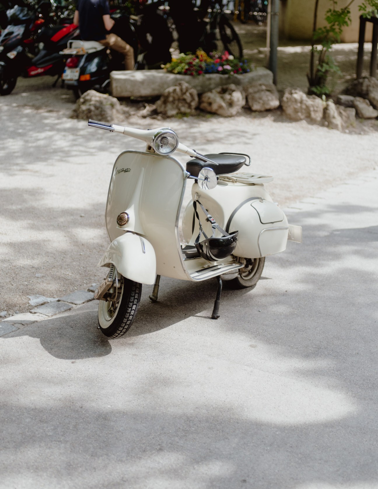 Cream-coloured vintage Vespa scooter parked on pavement outside a beer garden.