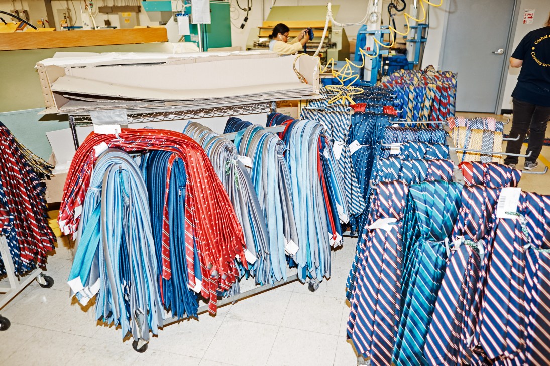 Colorful woven ties hanging on display racks in a New York factory production facility.
