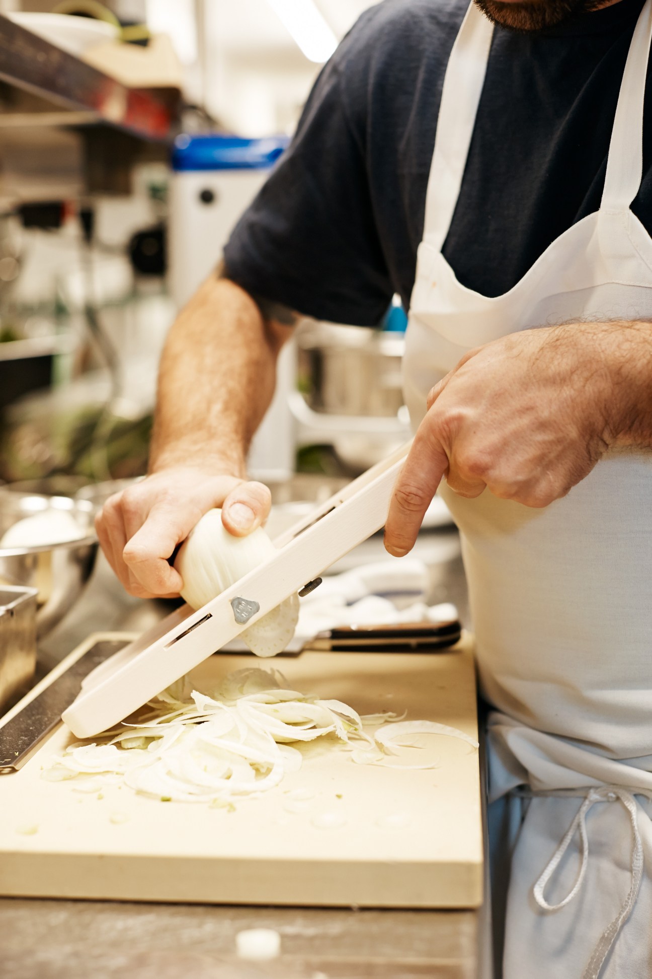Chef's hands slicing fennel bulb with a knife in a professional kitchen.