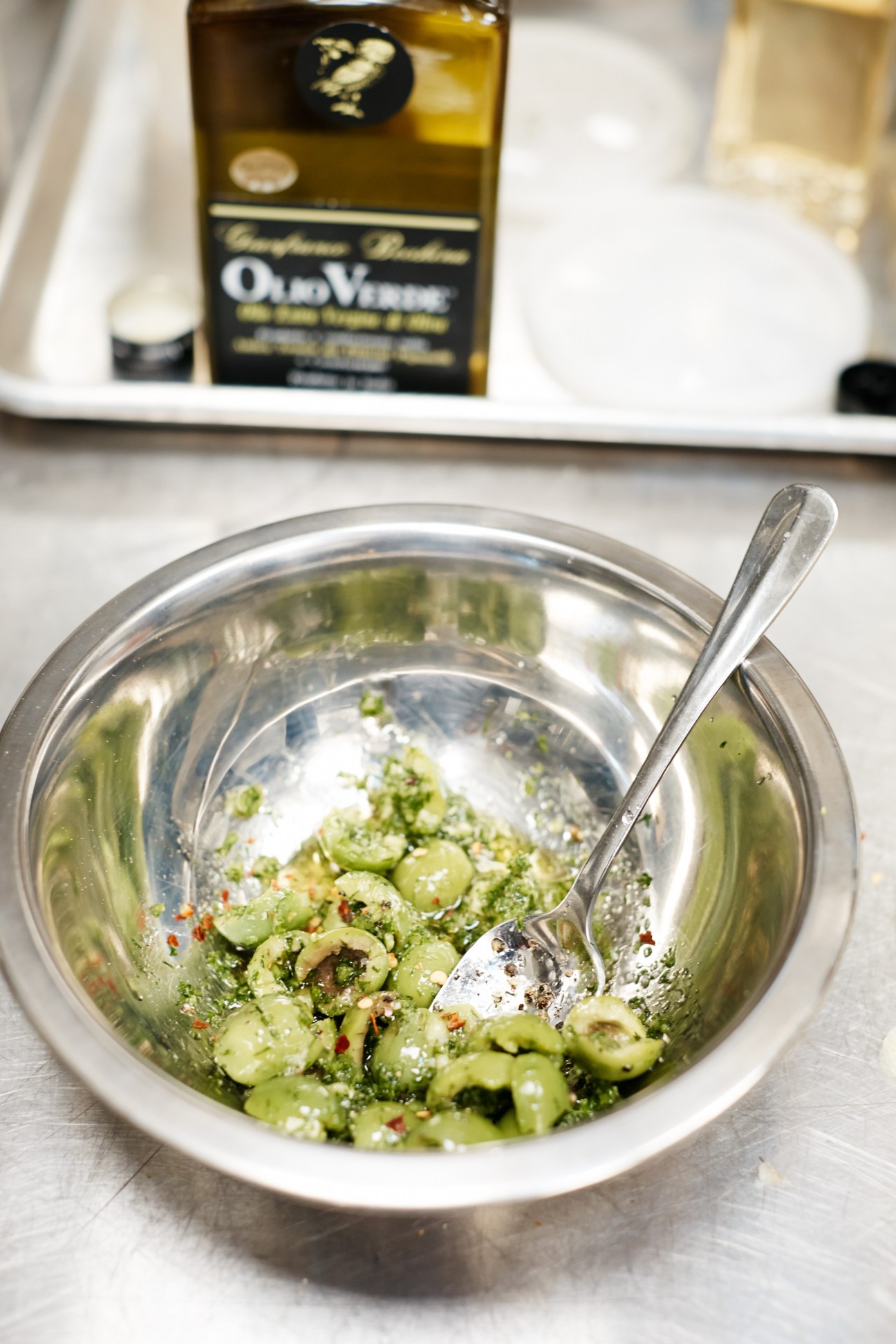 A bowl of fennel salad with chopped olives, chilli flakes and grated cheese, with olive oil bottle visible in background.