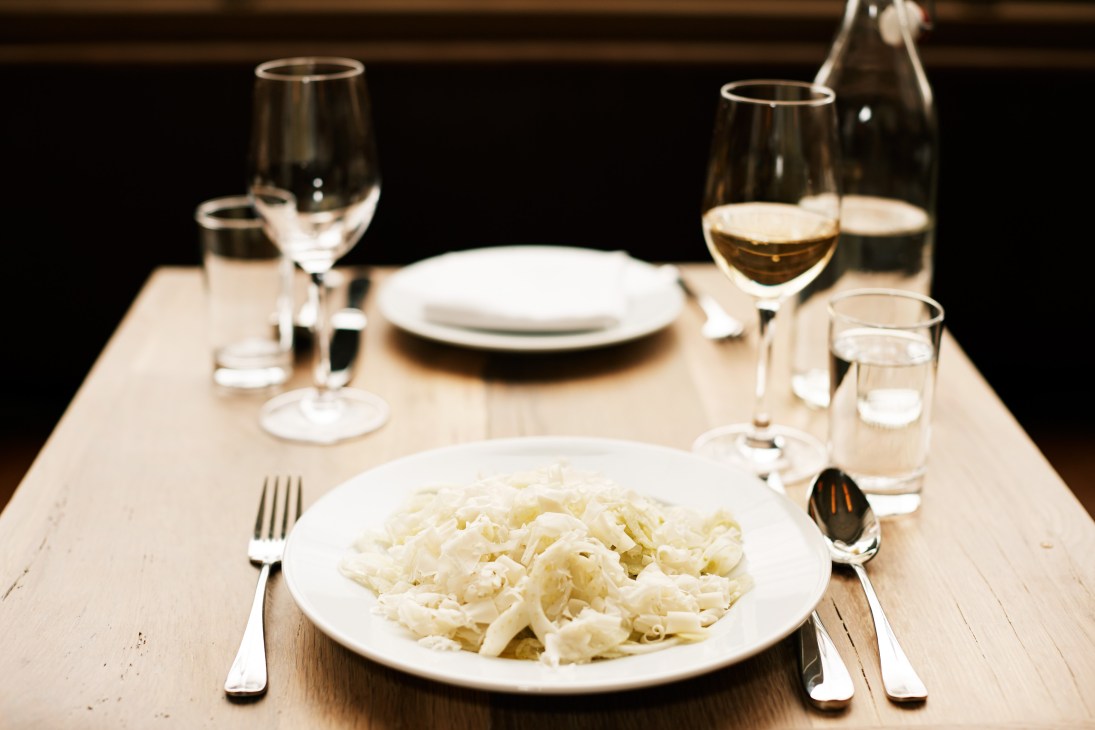 A plated fennel salad dish at Café Altro Paradiso with wine glasses and place settings on a light wood table.