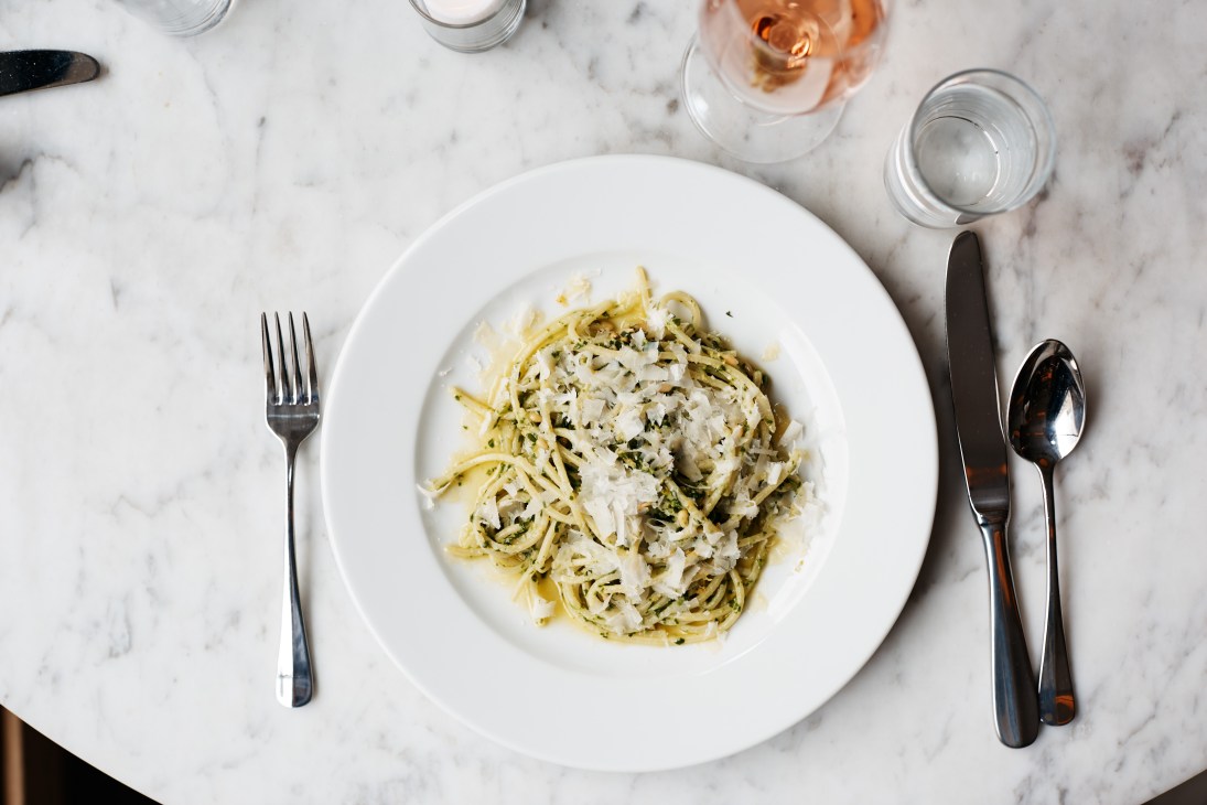 Spaghetti with ramp pesto served on a white plate atop marble, garnished with shaved cheese.