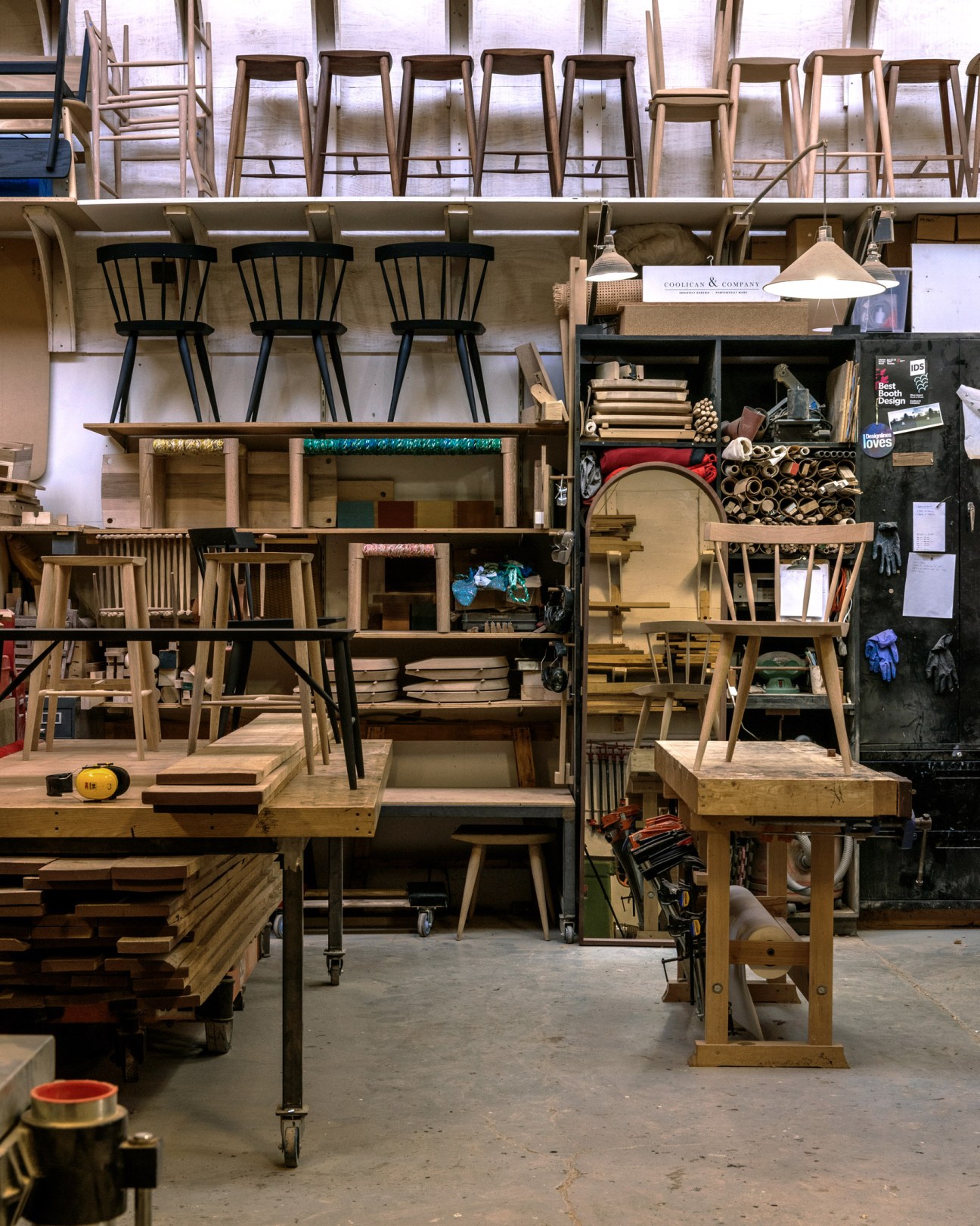 Coolican & Company's furniture workshop displaying wooden chairs, tables, and design materials on shelves.
