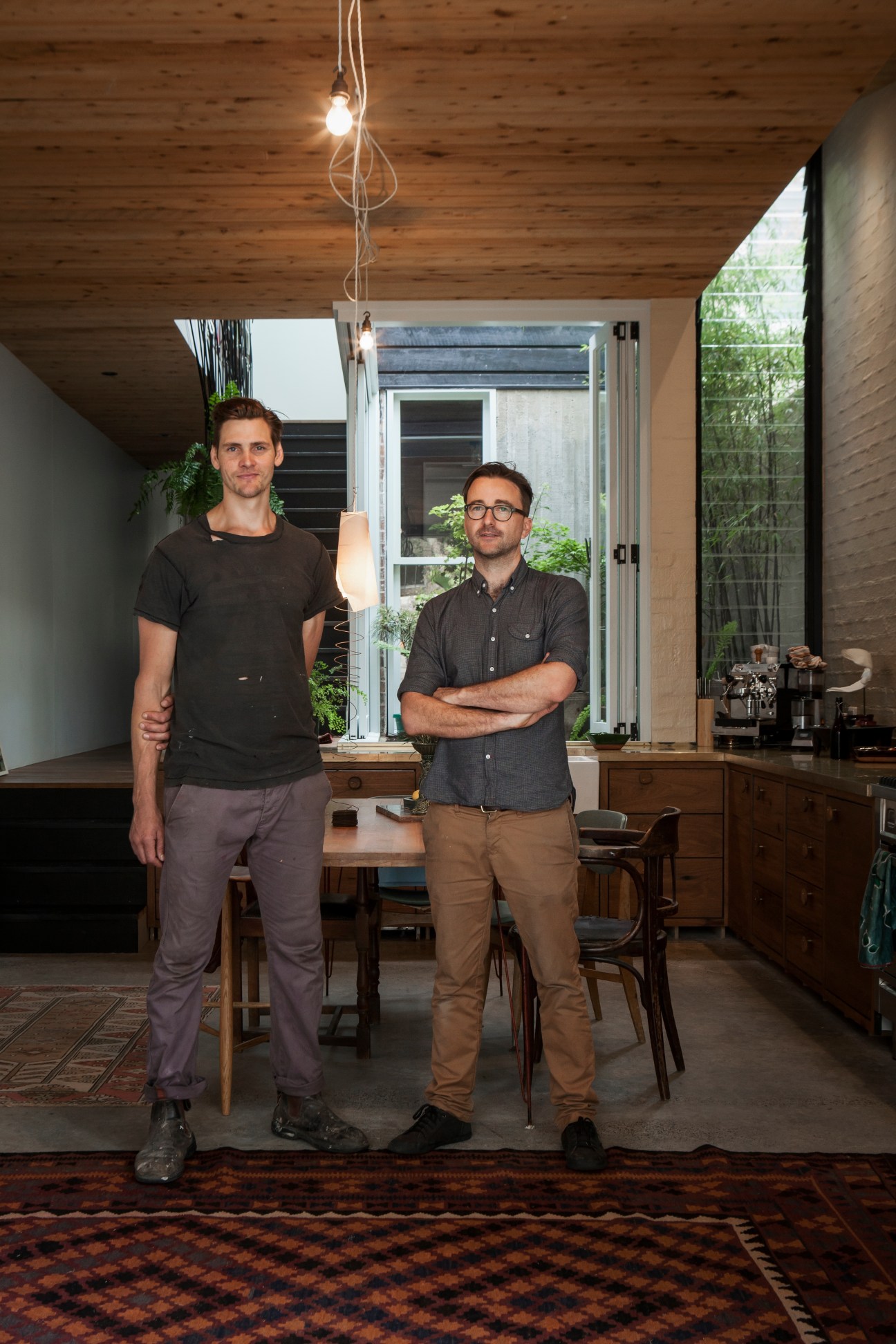 Jonathan West and Cameron Krone stand in a modern interior with wooden ceiling and pendant lights.