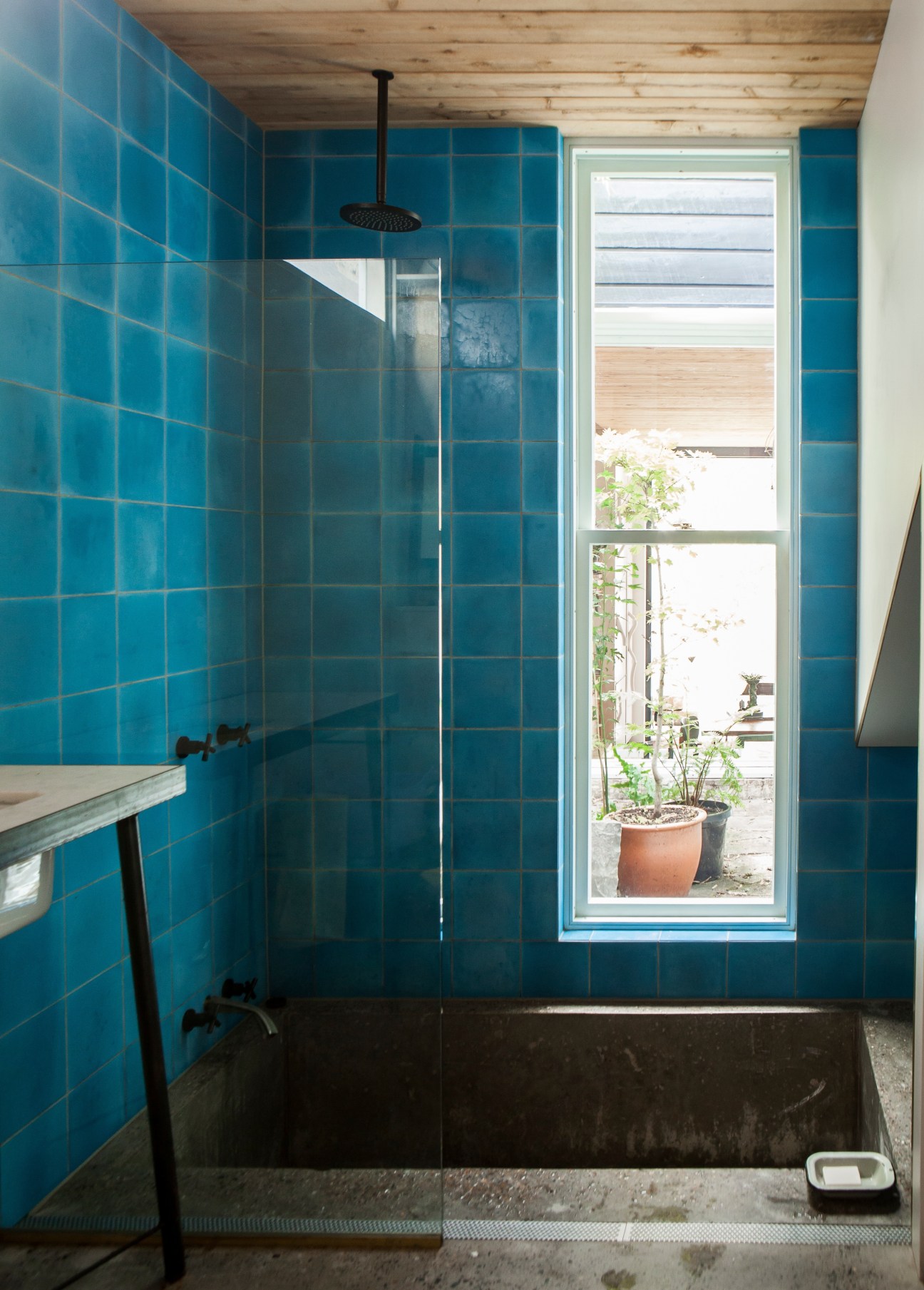 A bathroom with vibrant turquoise tiles, black fixtures, and a window overlooking a garden.
