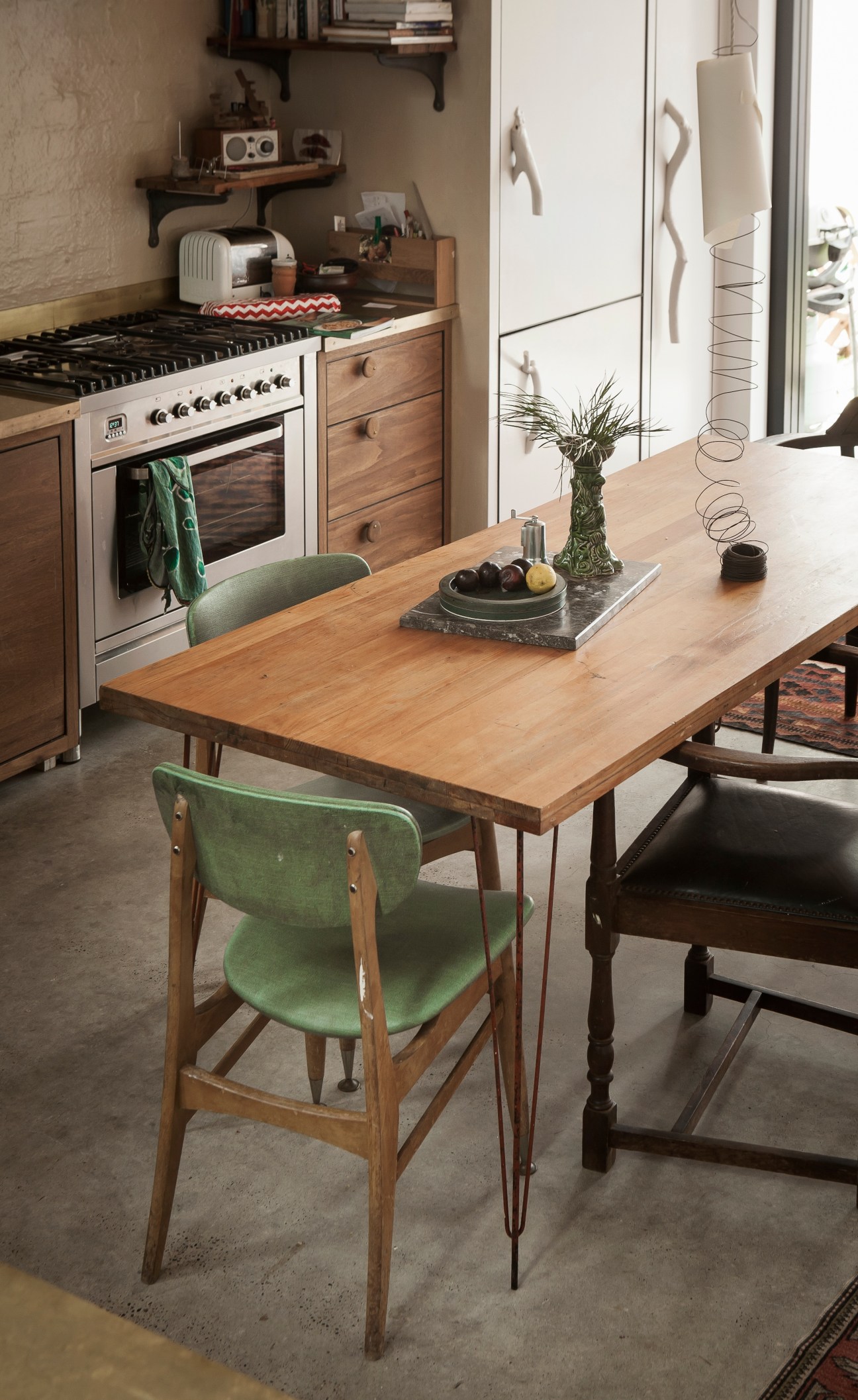 Modern kitchen with wooden table, green chair, stove, and shelving in a minimalist interior.